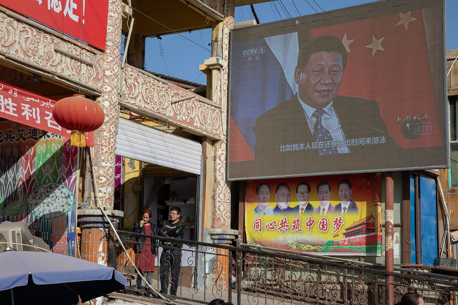 AP21020290036222.jpg 2017年11月3日,在中国新疆和田市集贸市场附近的屏幕上的习近平,下方宣传标语:同心共筑中国梦。 (美联社图片)
