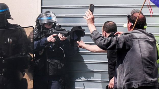 Police officer points a rubber bullet gun at protester