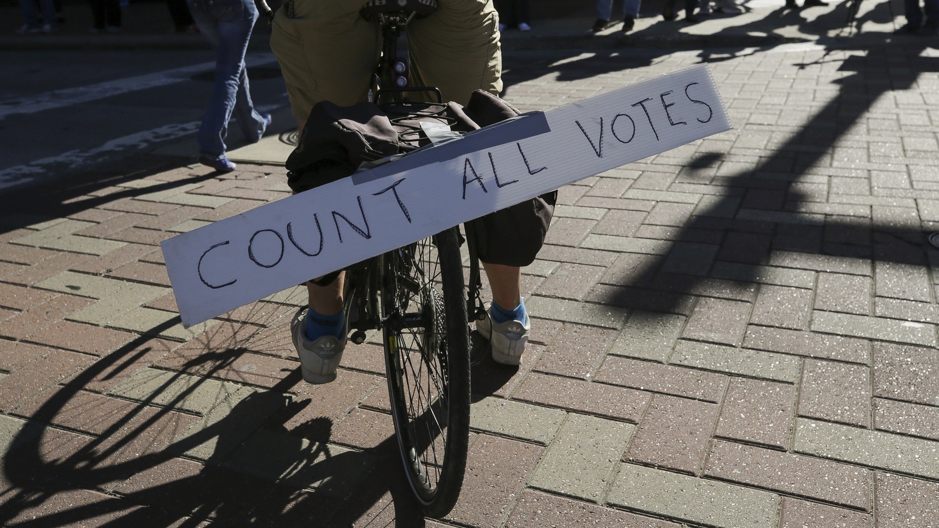 美國大選：圖為11月2日，德州民眾上街支持「免下車」投票，有人在單車上排寫有「點算所有選票」的標語牌。（AP）