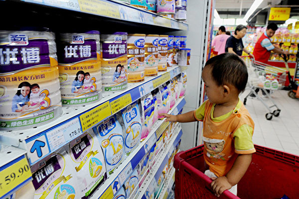 a chinese baby plays beside tins of milk